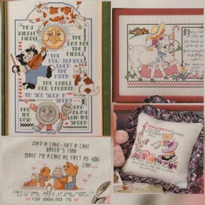May include: A collection of cross-stitch nursery rhyme samplers featuring Hey Diddle Diddle with a cat and fiddle, Mary Had a Little Lamb, Mary Mary Quite Contrary with a bear, and Pat-a-Cake with bears, all displayed in frames or as a pillow.