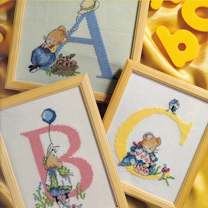 以下が含まれることがあります： 文字A、B、Cをあしらった3つのクロスステッチ刺繍作品。Aは青色でネズミ、Bはピンク色で風船を持つネズミ、Cは黄色でネズミと小鳥が描かれています。それぞれ明るい木製のフレームに入っています。
