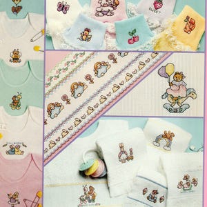 May include: A collection of baby apparel and fabric items featuring cross-stitch embroidery designs. The items include white, pink, and green onesies, lace-trimmed socks in pastel colors, and white towels with motifs of bears, rabbits, and text.