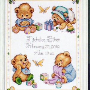 Könnte beinhalten: Kreuzstich-Kunstwerk mit vier Teddybären mit Babyzubehör. Das Kunstwerk enthält den Namen "Nicholas Ethan", das Geburtsdatum und das Gewicht. Die Bären sind von Schmetterlingen, Geschenken und Spielzeug umgeben, alles in Weiß gerahmt.
