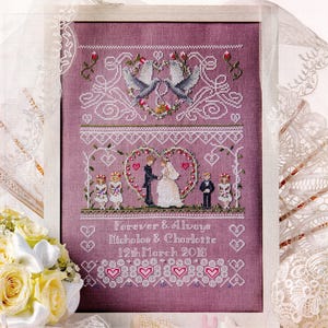 Può includere: Un ricamo a punto croce incorniciato su tessuto color malva con due colombe, una coppia di sposi all'interno di un cuore floreale e due coppie di bambini. Il testo recita: Forever & Always, Nicholas & Charlotte, 12th March 2016.