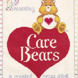 Puede incluir: Un patrón de punto de cruz sobre tela blanca que muestra un oso marrón con un corazón rosa en el vientre sentado sobre un gran corazón rojo. El texto dice P-resenting Care Bears in counted cross stitch con un borde colorido de pequeñas cruces.