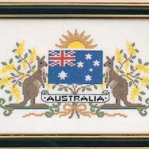 May include: Cross-stitch embroidery of the Australian coat of arms, featuring a blue shield with the Union Jack and Southern Cross, flanked by kangaroos and wattle branches. The word "AUSTRALIA" is stitched below. Framed in black.
