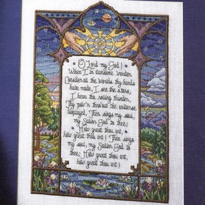 May include: A cross-stitch embroidery featuring a landscape scene with trees, flowers, and a pond, framed by a decorative border. At the top, two hands reach towards a celestial sphere. The centre contains the text of the hymn How Great Thou Art.