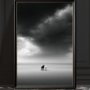 Pode incluir: Uma impressão de arte de parede emoldurada em preto e branco apresentando uma paisagem vasta e vazia sob um céu dramático e nublado. Dois cães pequenos, um preto e um branco, estão lado a lado no centro da linha do horizonte.