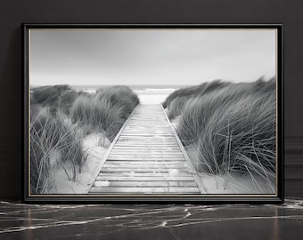 Puede incluir: Impresión en blanco y negro enmarcada de una escena de playa. Una pasarela de madera atraviesa dunas cubiertas de hierba que conducen al mar. La obra de arte se presenta en un marco negro, sobre un fondo oscuro.