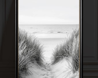 Puede incluir: Impresión enmarcada en blanco y negro de una escena de playa. Un sendero arenoso conduce al océano, enmarcado por altas hierbas. La obra de arte está en escala de grises, con un marco negro y un borde interior dorado, creando una estética minimalista.