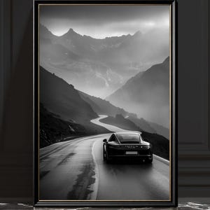 May include: Monochrome framed print featuring a black sports car on a wet, winding road through a mountainous landscape. The image captures a sense of movement and the dramatic scenery of the mountains.