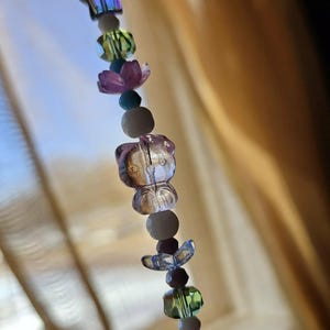 Puede incluir: Una pulsera de abalorios con cuentas iridiscentes en varias formas, incluyendo estrellas, flores y una figura de Hello Kitty. Las cuentas están ensartadas con un cordón transparente, creando un accesorio caprichoso y colorido.
