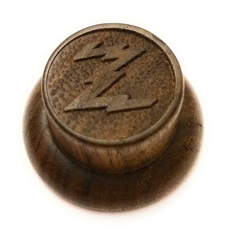 May include: A wooden knob with a stylized lightning bolt design. The knob is dark brown and has a smooth, polished finish.