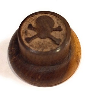 May include: A dark brown wooden knob with a skull and crossbones design carved into the top.