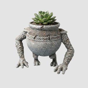 Puede incluir: Una maceta de cerámica de tono gris única con forma de criatura con brazos y piernas. La maceta contiene una suculenta verde. La maceta tiene una superficie texturizada con patrones decorativos. La URL de la tienda Etsy es visible.