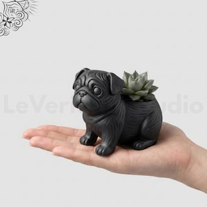 May include: A matte black pug-shaped planter featuring a sculpted dog with wrinkled facial features and a small green succulent plant nestled in the back. The planter is shown in a palm, with the text LeVeridianStudio.etsy.com at the bottom.