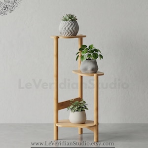 May include: A three-tiered bamboo plant stand with a light wood finish. The stand features three shelves holding potted plants: a top shelf with a grey chevron-patterned pot, a middle shelf with a grey ribbed pot, and a bottom shelf with a plain white pot.