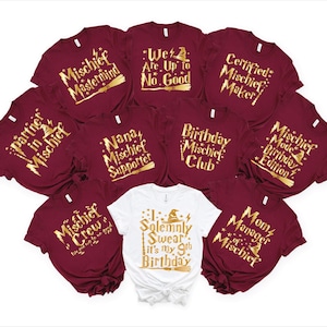 Peut inclure: Plusieurs t-shirts bordeaux et blancs avec des inscriptions dorées. On peut lire des phrases comme "Mischief Mastermind" et "I Solemnly Swear it's my 9th Birthday". Idéal pour une fête d'anniversaire à thème.
