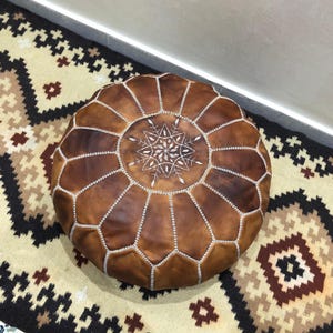 Round tan leather pouf with traditional stitching.
