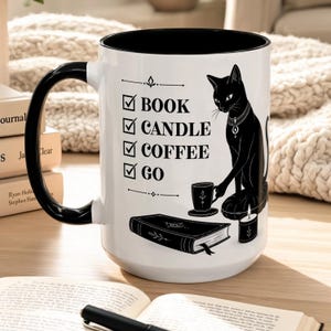 Peut inclure: Un mug en céramique blanche avec une anse et un bord intérieur noirs. Le mug présente un motif noir représentant un chat, un livre, une bougie et une petite tasse, accompagné d'une liste à cocher avec le texte : BOOK, CANDLE, COFFEE, GO.