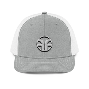 May include: A grey trucker cap with a white mesh back and a curved peak. The cap has a circular emblem with a stylized design in the centre. The emblem is embroidered in a lighter shade of grey.