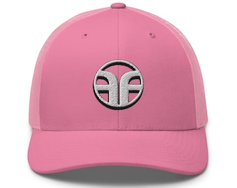 Puede incluir: Una gorra tipo trucker de color rosa brillante con un panel frontal estructurado y una parte trasera de malla transpirable. En el centro de la parte frontal hay un logotipo circular bordado en blanco y negro con un diseño geométrico estilizado que recuerda a las letras AF.