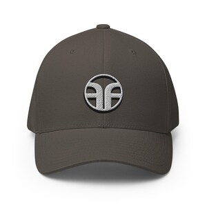 May include: A dark gray baseball cap with a curved brim. The cap features a white embroidered logo on the front, a stylized design within a circle. The cap is made of a soft material and has a structured fit.
