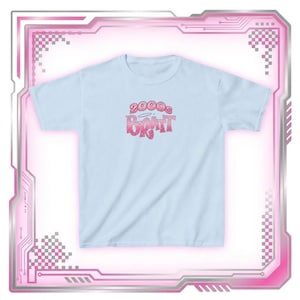 May include: A light blue t-shirt with the text "2000s Bratt" in a pink gradient font. The shirt has short sleeves and a crew neck. The design is centered on the front of the shirt.
