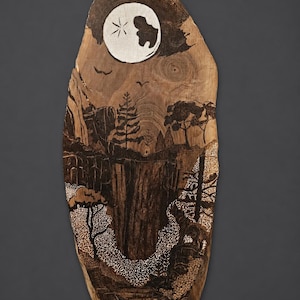May include: A wood-burned art piece depicting a nighttime landscape. The artwork features a full moon with a star, trees, mountains, and a river. The piece is on a natural wood slab with a dark brown finish.