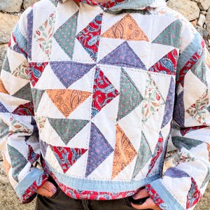 May include: A hooded pullover constructed from quilted fabric featuring a patchwork design of triangular segments. The pattern includes various prints in shades of red, orange, green, blue, and white, with visible stitching throughout the garment.