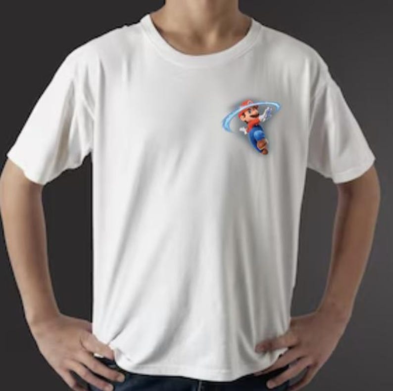 Puede incluir: Camiseta blanca de manga corta con un gr&aacute;fico colorido de un personaje de dibujos animados con gorro rojo y peto azul. El personaje est&aacute; rodeado por un dise&ntilde;o de remolino azul. La camiseta est&aacute; hecha de un material suave y ligero.