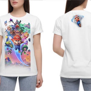 Puede incluir: Camiseta blanca con un gr&aacute;fico colorido de Mario y otros personajes de la serie Super Mario Bros. La parte delantera de la camiseta muestra una escena vibrante con m&uacute;ltiples personajes. La parte trasera de la camiseta tiene una imagen m&aacute;s peque&ntilde;a de Mario.