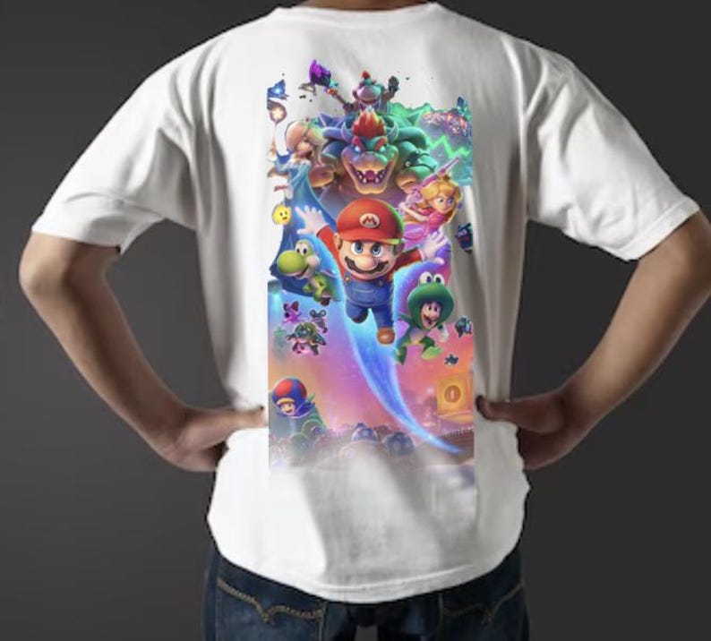 Puede incluir: Camiseta blanca con un gr&aacute;fico colorido de Mario y otros personajes de la serie de videojuegos Super Mario. El dise&ntilde;o incluye a Mario, Bowser, la Princesa Peach y varios otros personajes en una escena din&aacute;mica y llena de acci&oacute;n.