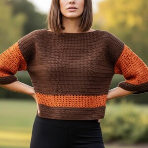 May include: A brown and orange crochet sweater with short sleeves. The top is primarily brown with orange sleeves and a horizontal orange stripe at the waist. The sweater has a boat neck and is made of a textured yarn.