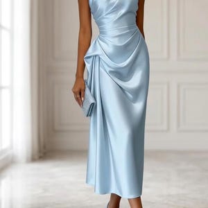 May include: A light blue, one-shoulder satin dress with draped detailing. The dress has a fitted bodice and a knee-length skirt. A matching clutch and heels complete the look. The dress is suitable for formal events.