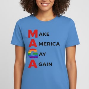 Puede incluir: Camiseta azul claro con el texto "MAKE AMERICA GAY AGAIN" en rojo y negro. La palabra "GAY" está en colores del arcoíris. La camiseta es de cuello redondo y manga corta.