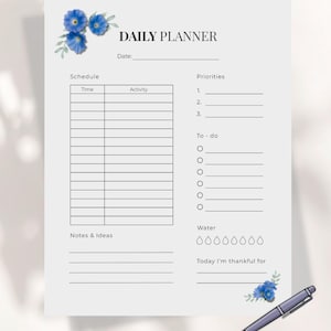 Puede incluir: Un planificador diario blanco con el texto "DAILY PLANNER" y secciones para programación, prioridades y notas. Incluye detalles florales azules y un bolígrafo. Diseñado para uso digital.
