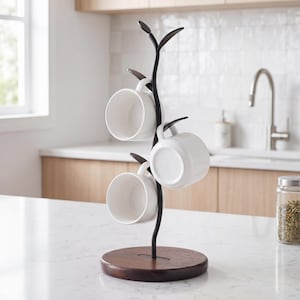 May include: A black metal mug tree with a dark brown wooden base holds four white ceramic mugs. The tree has a branch-like design with leaf-shaped accents at the top. The mugs are evenly spaced and ready for use.