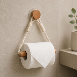 Könnte beinhalten: Ein wandmontierter Toilettenpapierhalter mit einer runden Basis aus hellem Holz, einem passenden Holzstab und einem dicken, cremefarbenen, gedrehten Baumwollseil. Das Seil ist durch die Holzenden geführt, um die weiße Toilettenpapierrolle zu halten.