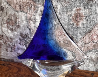 May include: A glass sculpture shaped like a sailboat, featuring a clear glass base and a triangular sail section that transitions from a deep, vibrant blue at the bottom to a transparent, clear glass at the top, creating a smooth gradient effect.