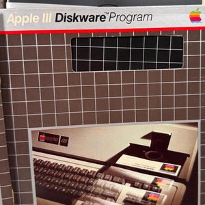 Puede incluir: Un disquete vintage Apple III Diskware Program y su funda de cart&oacute;n. La funda presenta un patr&oacute;n de cuadr&iacute;cula marr&oacute;n, el texto Apple III Diskware Program y una foto de un teclado de computadora Apple III.