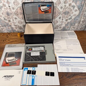 May include: An Apple SoftCard III system set including a black storage box, a Microsoft BASIC manual, a packing list, a floppy disk in a gray tray, a sheet of labels, and a registration form. The manual cover features an image of an Apple computer.