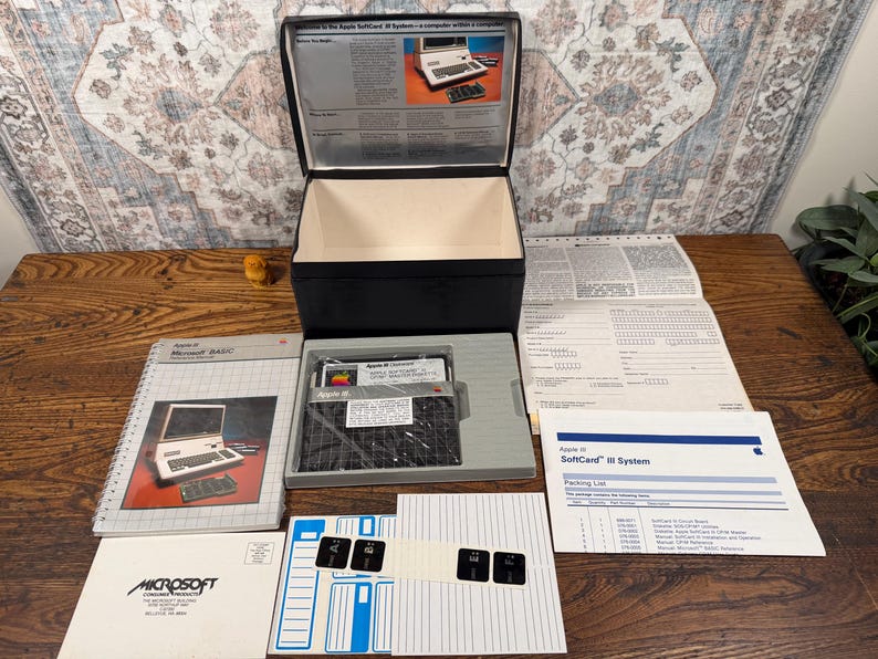 May include: An Apple SoftCard III system set including a black storage box, a Microsoft BASIC manual, a packing list, a floppy disk in a grey tray, a sheet of labels, and a registration form. The manual cover features an image of an Apple computer.