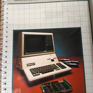 May include: A spiral-bound Apple III Microsoft BASIC Reference Manual with a white cover featuring a grid pattern. The cover displays an illustration of an Apple III computer, several floppy disks, and a circuit board on a dark red surface.
