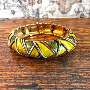 May include: A hinged bangle bracelet featuring a series of interlocking, triangular segments finished in a glossy, vibrant chartreuse and olive green enamel. The metal frame is gold-toned, showcasing a textured, metallic finish on the interior.