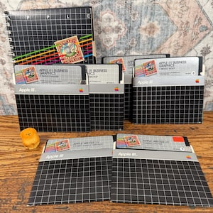 May include: A collection of vintage Apple III software floppy disks and a spiral-bound manual. The black sleeves feature a white grid pattern and the Apple III logo. Labels include Apple III Business Graphics and Apple Writer III software titles.