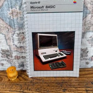 May include: A spiral-bound Apple III Microsoft BASIC Reference Manual with a white cover featuring a grid pattern and a central photograph of an Apple III computer, keyboard, and circuit board. The Apple logo is visible in the top right corner.