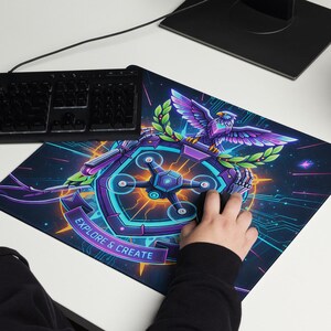 May include: A rectangular mouse mat with a vibrant design featuring a purple and blue eagle, a shield, and the text "EXPLORE & CREATE." The mouse mat is on a white desk next to a keyboard and monitor.