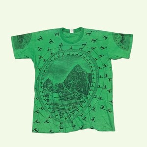 May include: Green t-shirt featuring a graphic of Machu Picchu, the Incan citadel in Peru, surrounded by a circle of llamas. The shirt also has the text "Machu Picchu, The Inka City Cusco Peru, La Nueva Maravilla Del Mundo."