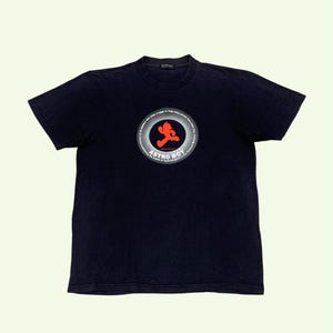 May include: A white ceramic mug with a black handle and the text "But First, Coffee" in a bold, black font. The mug is filled with a dark liquid, likely coffee, and sits on a light-colored surface.