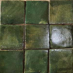 May include: A grid of nine square tiles featuring a glossy, deep forest green glaze. Each tile displays unique variations in color saturation, surface texture, and light reflection, creating a mottled appearance across the entire arrangement.