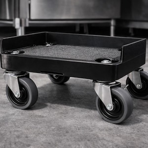 May include: A black utility cart with four gray wheels. The cart has a rectangular base with a textured surface and raised edges. The wheels are mounted on silver brackets.