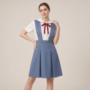 Completo composto da grembiule blu, camicetta bianca, fiocco bordeaux e gonna a pieghe, ispirato a un'uniforme scolastica.